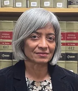 Bhamati Viswanathan is in front of legal books.  She is wearing a black jacket and smiling slightly.