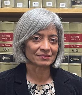 Bhamati Viswanathan is in front of legal books. She is wearing a black jacket and smiling slightly.